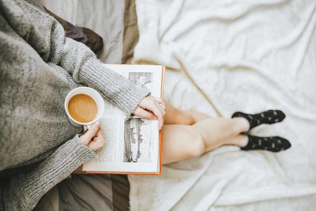 girl reading a book while holding a cup of coffee