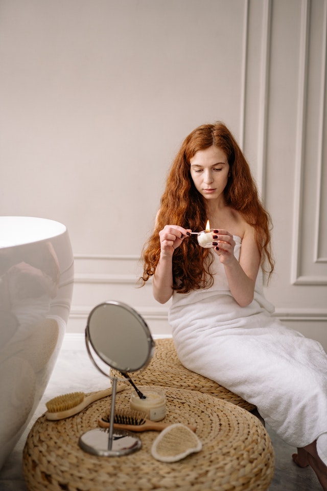 girl sitting by bathtub and lighting a candle